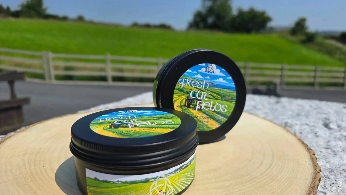 Two Fresh Cut Fields candle tins on a wood slice outdoors, fields behind