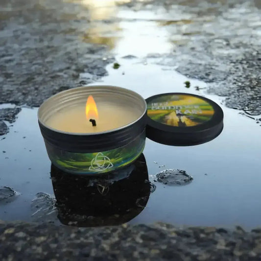 Lit Irish Summer Rain tin candle sitting in a rain puddle