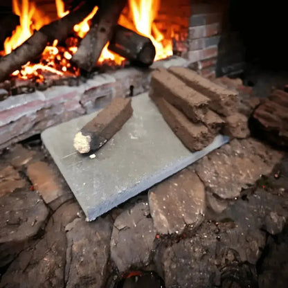 Turf incense sods on a grey slate in a stone hearth, one sod lit, a fire burning behind