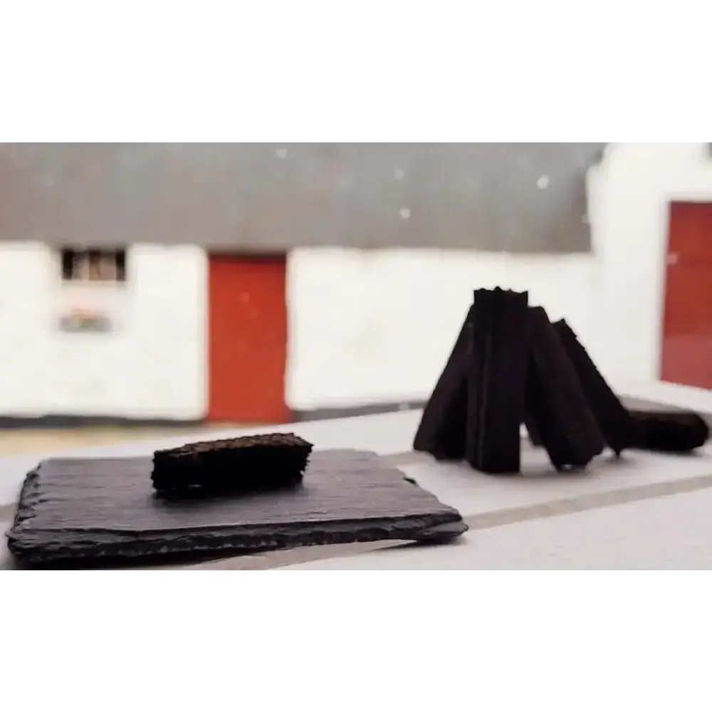 Dark turf sod on a black slate with sods stood in a cone, white cottage with red door behind