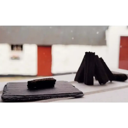 Dark turf sod on a black slate with sods stood in a cone, white cottage with red door behind