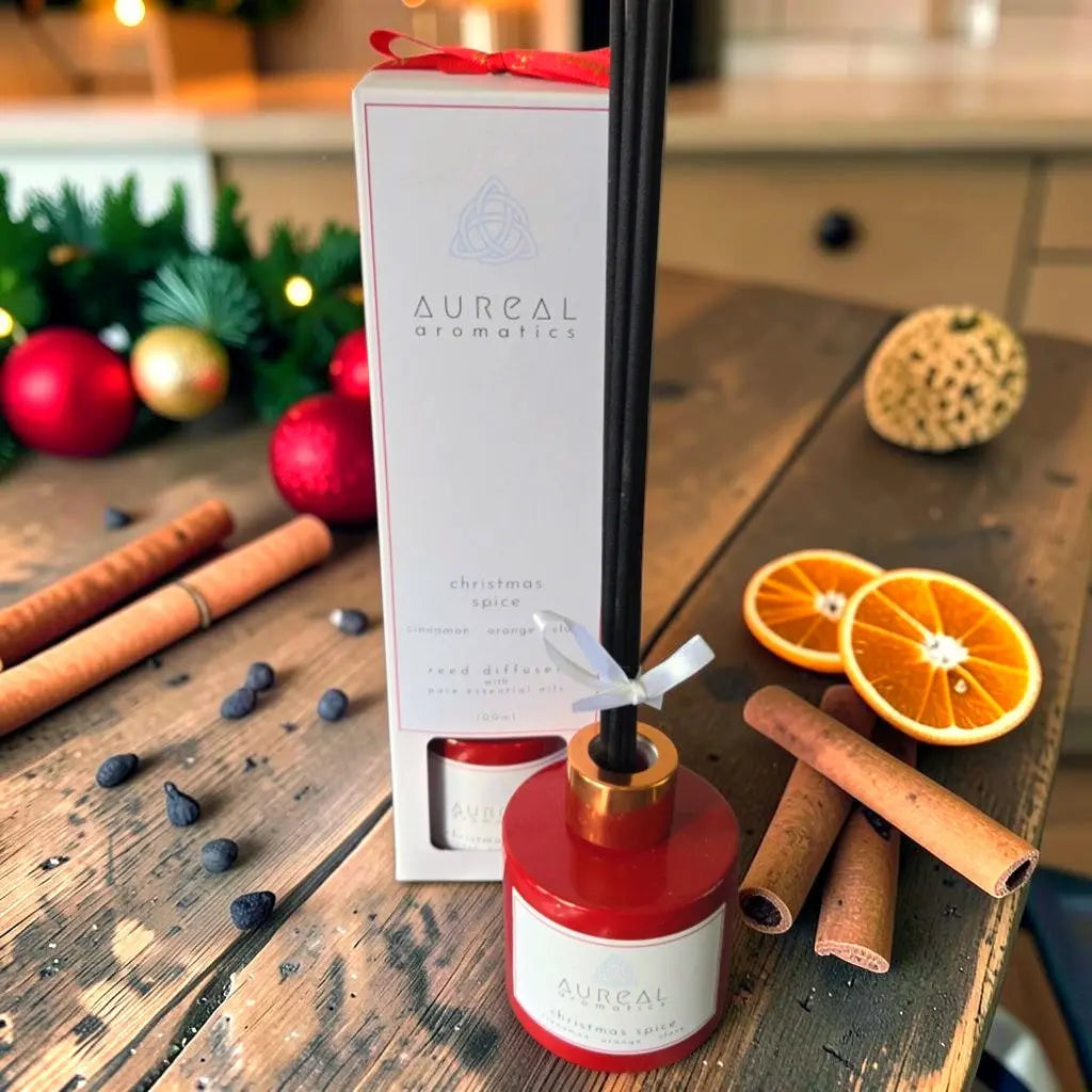 Aureal Christmas Spice reed diffuser in a red bottle with black reeds, its box and cinnamon