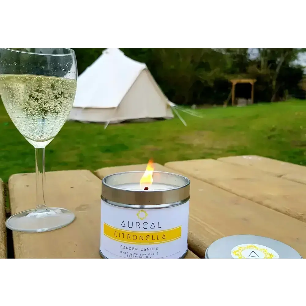 Lit Citronella garden candle on a picnic table with a glass of wine and a bell tent behind