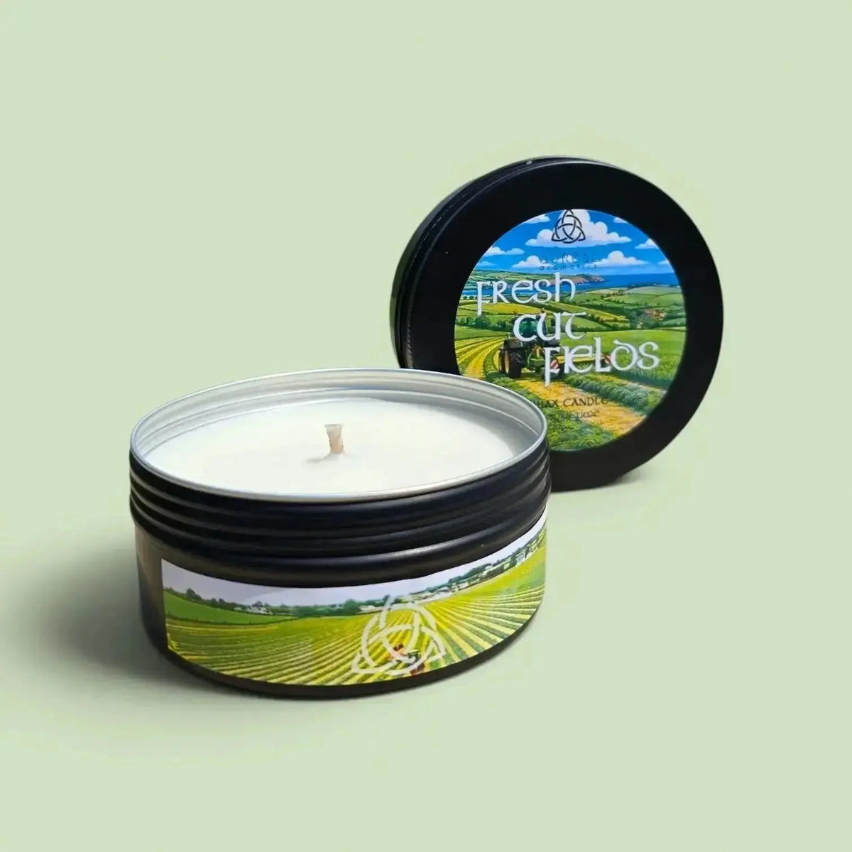 Fresh Cut Fields candle in a black tin with its lid, on a pale green background