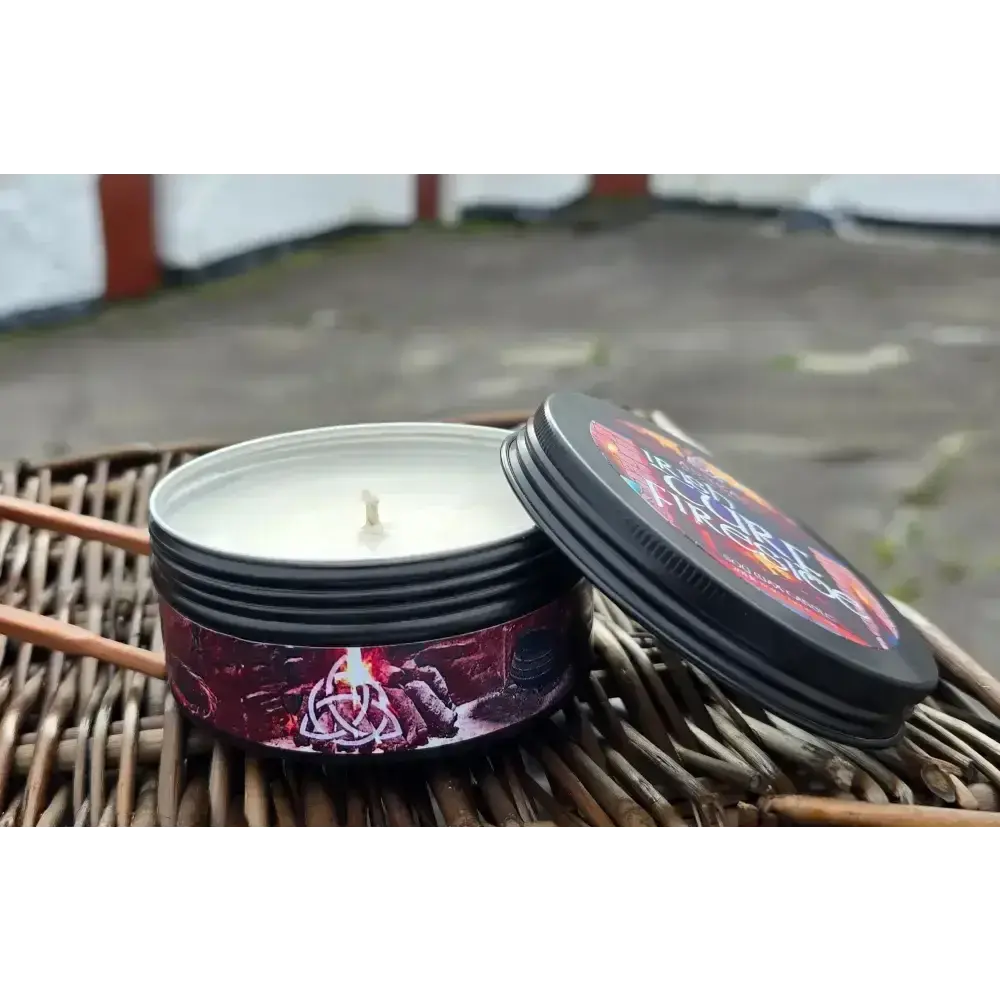 Candle in a black tin with a red label and its lid, on a wicker basket