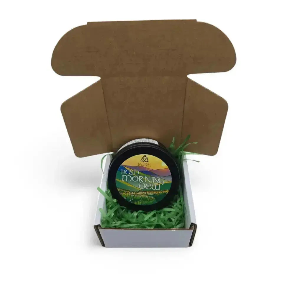 Irish Morning Dew candle tin in an open brown mailer box with green paper shred