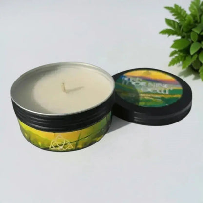 Irish Morning Dew candle in a black tin with its lid beside it and a fern