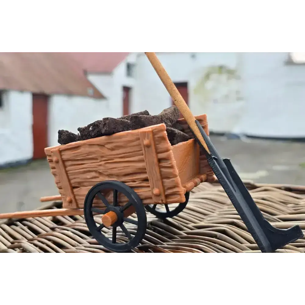Miniature turf cart filled with turf sods and a turf spade, on wicker with white cottages behind