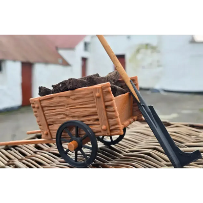 Miniature turf cart filled with turf sods and a turf spade, on wicker with white cottages behind
