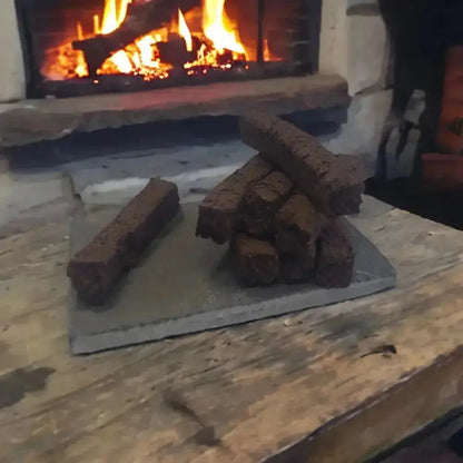 Turf incense sods stacked on a slate on a wooden table, with a lit fire behind