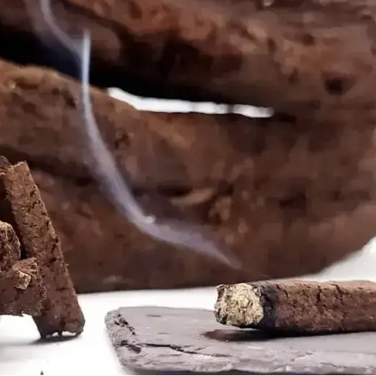 Close up of a turf incense sod smouldering on dark slate, with thin smoke rising