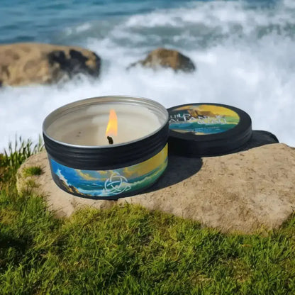 Lit tin candle with a seascape label on a rock by the sea, lid beside it