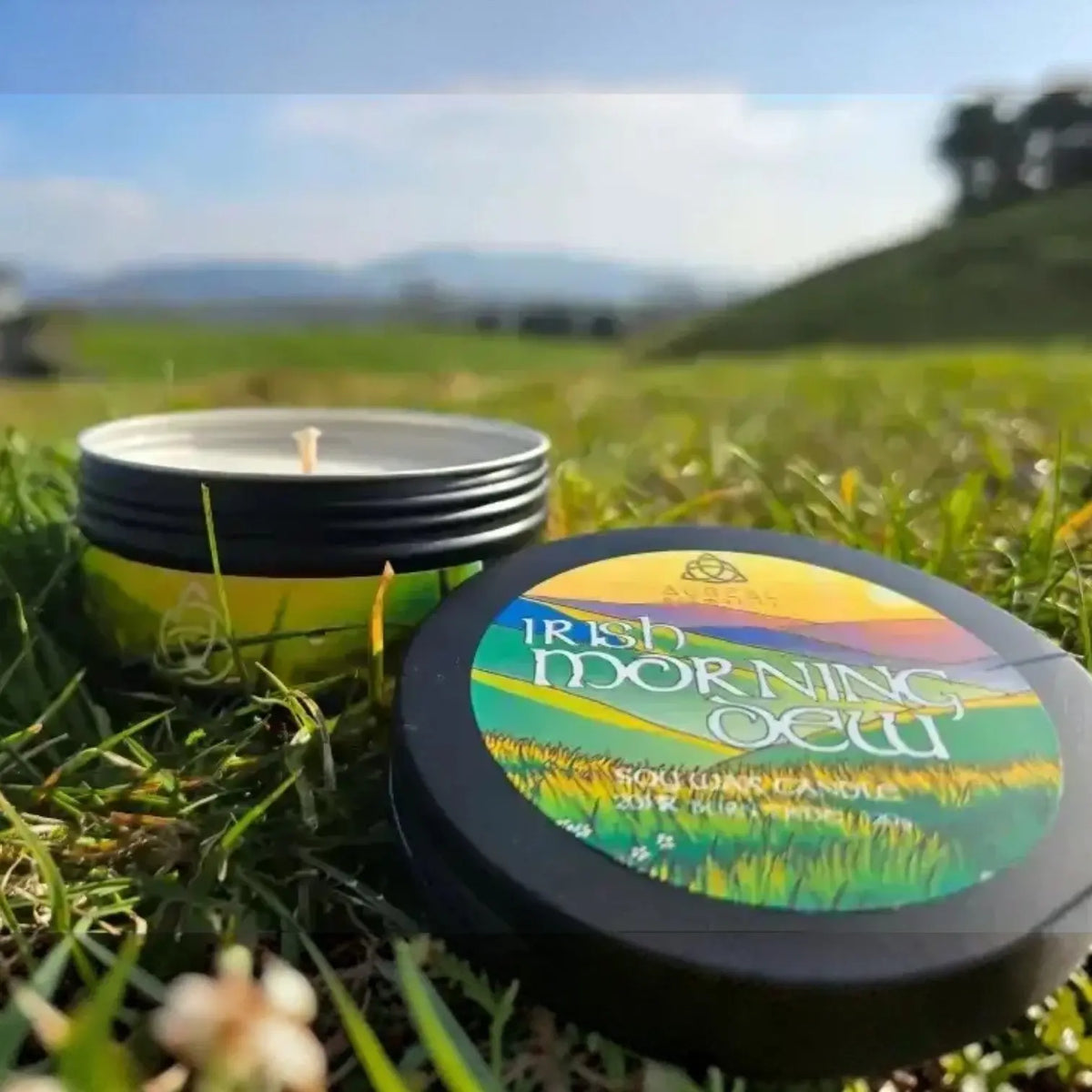 Irish Morning Dew tin candle and lid on grass with green hills behind